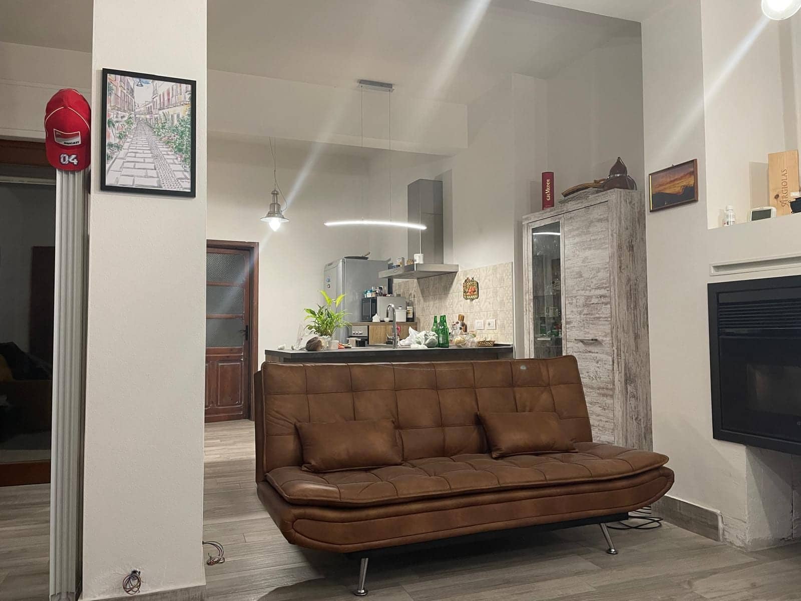 Soggiorno con divano in pelle marrone e camino, aperto sulla cucina con penisola e cappa in acciaio